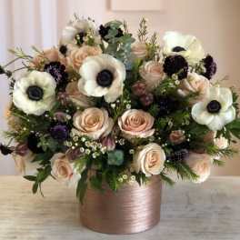 Arrangement of blush roses, white anemones, and dark blooms in a rose gold cylinder vase