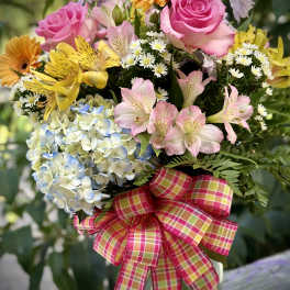 Mixed bouquet with pink roses, yellow flowers, and blue hydrangea in a glass vase