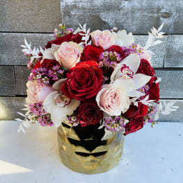 Bouquet of red and blush roses with white orchids in a gold mask vase