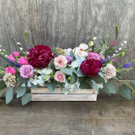 Low floral arrangement with pink and burgundy blooms in a wooden box
