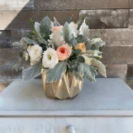 Compact bouquet of pastel roses and white blooms in a gold vase