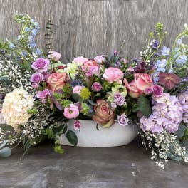 Low floral centerpiece with pink roses, lavender hydrangeas, and blue delphinium in a white bowl