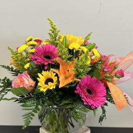 Bright mixed bouquet in a glass vase with pink gerberas, sunflowers, and lilies