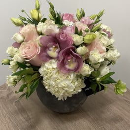 Low round arrangement of pink roses, white hydrangeas, and lavender orchids in a dark bowl vase