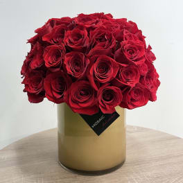 Dense arrangement of red roses in a cylindrical tan glass vase