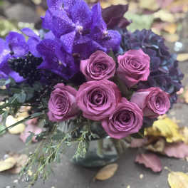 Purple orchids and pink roses arranged in a glass vase