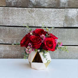 Red roses arranged in a geometric white vase with small pink filler flowers