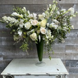 White floral arrangement in a tall green vase with cascading stems