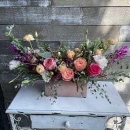 Mixed bouquet of pink, peach, and white flowers in a pink rectangular vase