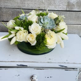 White roses and succulents arranged in a low green bowl