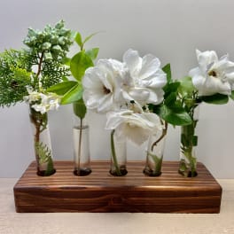 White flowers and greenery arranged in small glass tubes on a wooden base.