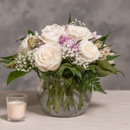 White rose bouquet in a glass vase with a small candle beside it