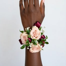 Peach rose wrist corsage with burgundy ribbon on a wrist