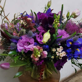Large mixed bouquet of purple, pink, and blue flowers in a glass vase