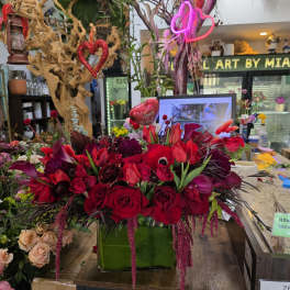 Red and burgundy floral arrangement in a green box with heart decorations