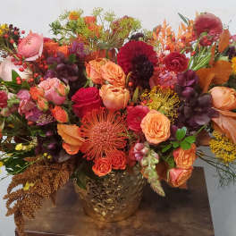 Large autumn bouquet with orange, red, and pink flowers in a gold vase