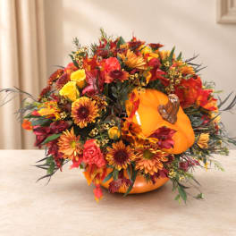 Autumn floral arrangement in a pumpkin-shaped container with orange and red blooms