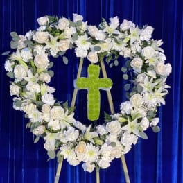 Heart-shaped white floral wreath with a green cross on an easel