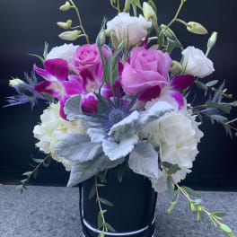 Pink roses and white blooms in a black hatbox with purple orchids