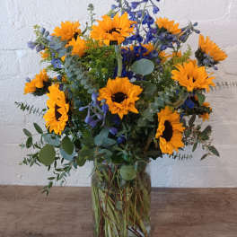 Sunflowers and blue flowers in a clear glass vase