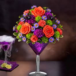 Colorful bouquet of roses, carnations, and daisies in a purple martini glass