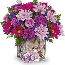 Pink and purple mixed bouquet in a square glass vase with a hummingbird design