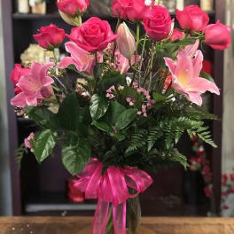 Pink roses and lilies arranged in a glass vase with a pink ribbon