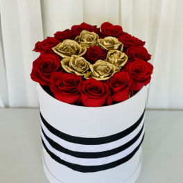 Red and gold roses arranged in a round white box with black stripes