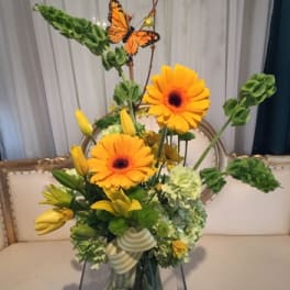 Yellow floral arrangement with orange gerbera daisies in a glass vase