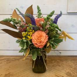 Peach roses in a dark glass vase with purple and yellow flowers