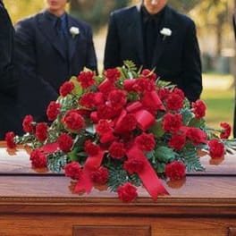 Red carnation casket spray with ribbon on a wooden casket