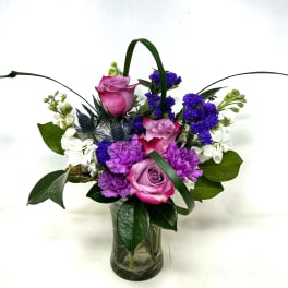 Pink and purple roses with white and blue flowers in a glass vase