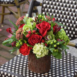 Rustic low arrangement of red roses and green blooms in a wood-look vase