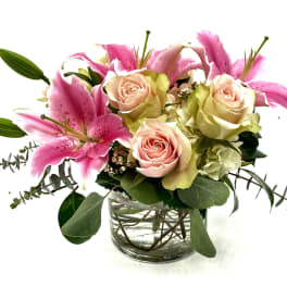 Pink lilies and pale roses arranged in a clear glass vase