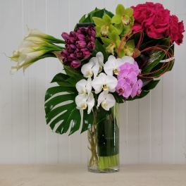 Mixed bouquet with orchids, roses, calla lilies, and tulips in a glass vase