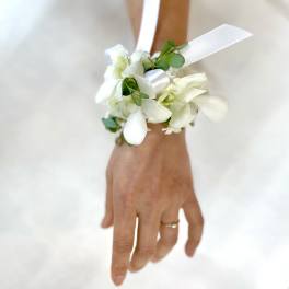 White orchid wrist corsage with ribbon on a person’s hand
