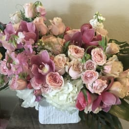 Large pink and peach floral arrangement in a white vase