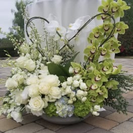 Large floral arrangement with white roses and green orchids in a low bowl