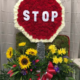 Large floral stop-sign tribute with red and white flowers and sunflowers below