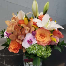 Mixed bouquet of orange roses, orchids, lilies, and hydrangea in a glass vase