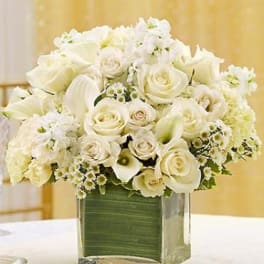 White roses and calla lilies arranged in a clear square vase