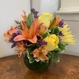 Bouquet of orange lilies and yellow roses in a green glass vase