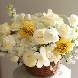 White floral arrangement in a wicker basket with yellow accents