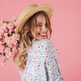 Smiling woman in a straw hat with a bouquet of pink carnations