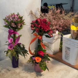 Three floral arrangements in buckets, including pink and red bouquets with ribbons