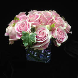 Low arrangement of pink roses with ivy accents in a clear glass cube vase