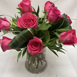 Short arrangement of hot pink roses with looped green leaves in a clear glass vase.