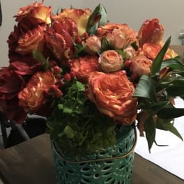 Orange and peach roses arranged in a teal ceramic vase