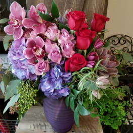 Bouquet of pink orchids, roses, hydrangeas, and succulents in a purple vase