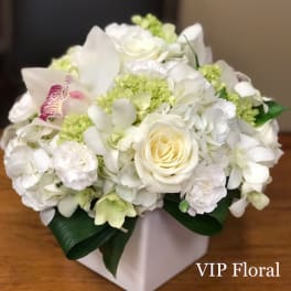 White floral arrangement in a square vase with pale green accents